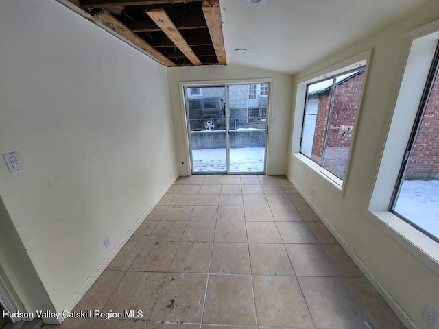 tiled spare room featuring a healthy amount of sunlight and vaulted ceiling