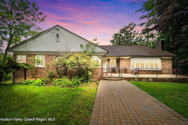 view of front of house with fence, a chimney, a lawn, and brick siding