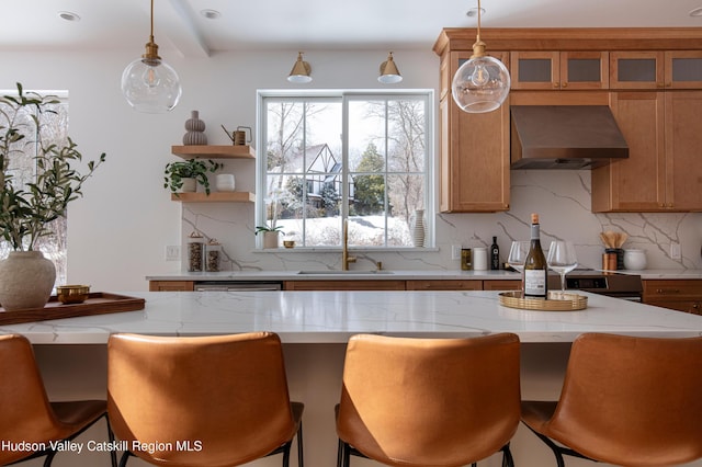 kitchen featuring a sink, wall chimney range hood, backsplash, a kitchen bar, and glass insert cabinets