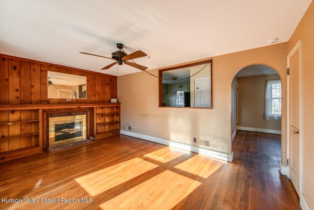 unfurnished living room with hardwood / wood-style flooring, ceiling fan, and wood walls