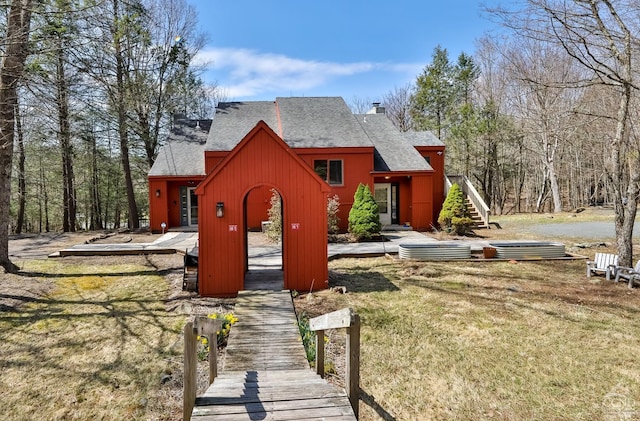 rear view of property featuring a chimney, a shingled roof, stairs, and a lawn