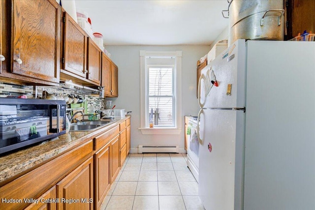 kitchen with light tile patterned floors, a baseboard radiator, freestanding refrigerator, a sink, and backsplash