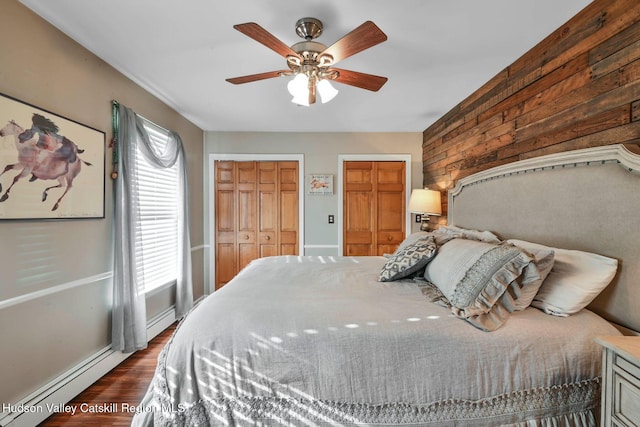 339-345 Jessup Rd, Florida, NY 10921 - bedroom with two closets, wooden walls, dark wood-style floors, a ceiling fan, and a baseboard heating unit