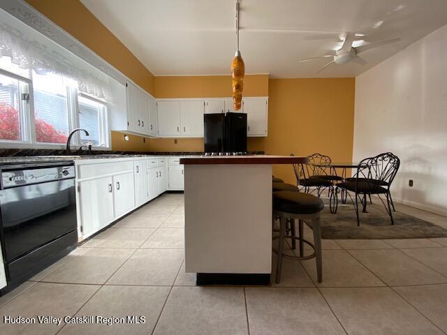 kitchen with pendant lighting, white cabinets, black appliances, and light tile patterned floors