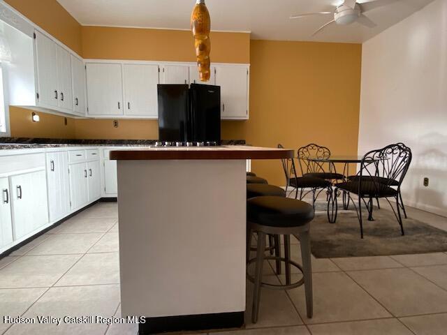 kitchen featuring black fridge, a breakfast bar, white cabinets, and light tile patterned floors