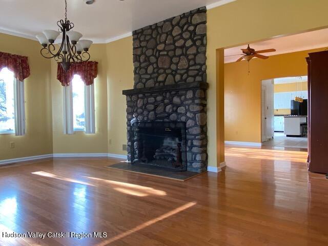 unfurnished living room with a fireplace, ornamental molding, ceiling fan with notable chandelier, and hardwood / wood-style flooring