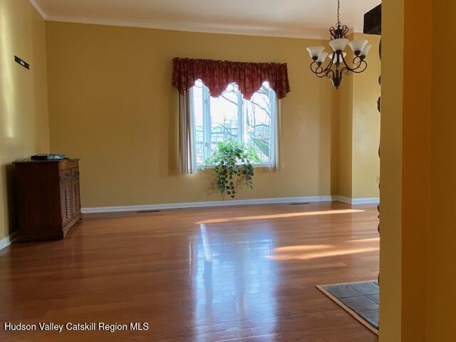 unfurnished room with crown molding, wood-type flooring, and an inviting chandelier