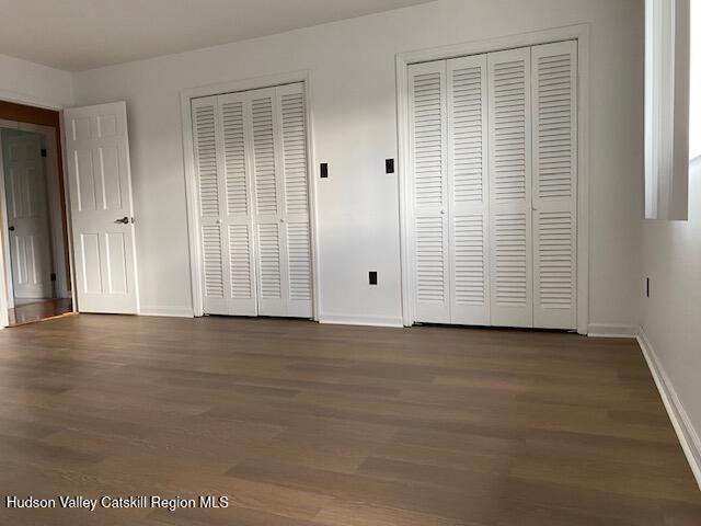 unfurnished bedroom with dark hardwood / wood-style flooring and multiple closets