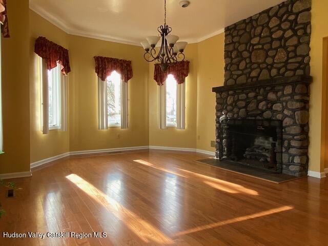 unfurnished living room featuring hardwood / wood-style floors, a stone fireplace, ornamental molding, and a chandelier