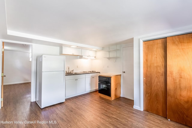 kitchen with freestanding refrigerator, white cabinets, a sink, wood finished floors, and oven