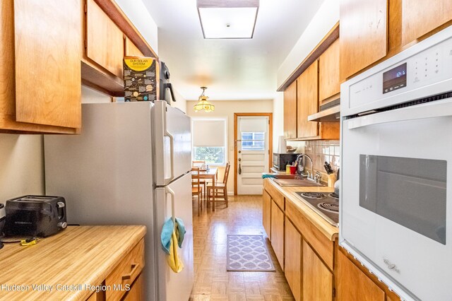 kitchen with light countertops, decorative backsplash, a sink, white appliances, and under cabinet range hood