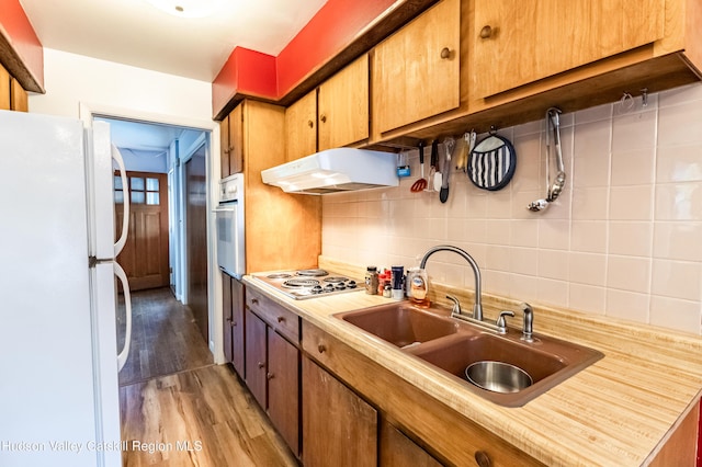 kitchen with white appliances, decorative backsplash, light wood-style floors, under cabinet range hood, and a sink