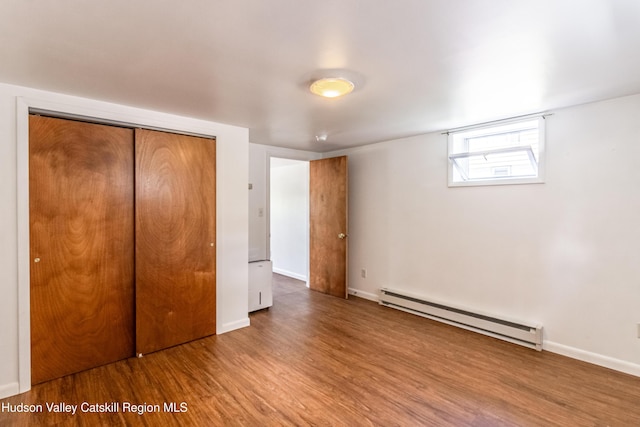 unfurnished bedroom featuring a closet, baseboards, baseboard heating, and wood finished floors