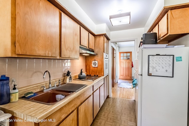 kitchen featuring under cabinet range hood, white appliances, a sink, light countertops, and tasteful backsplash