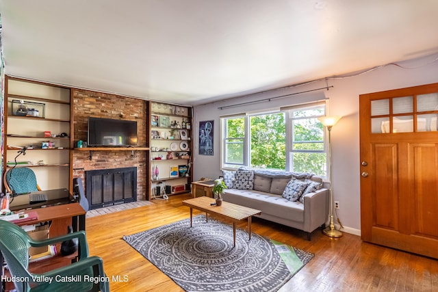 living room featuring built in shelves, wood-type flooring, a fireplace, and baseboards