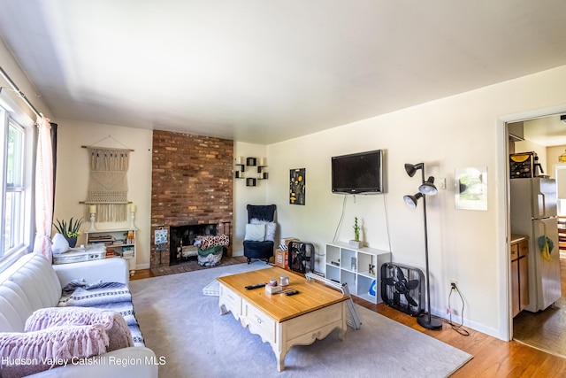 living area featuring a brick fireplace, baseboards, and light wood finished floors