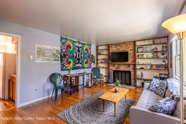 living area featuring built in shelves, a fireplace, baseboards, and wood finished floors