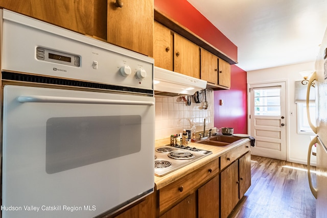 kitchen featuring tasteful backsplash, wood finished floors, white oven, a sink, and stainless steel electric stovetop