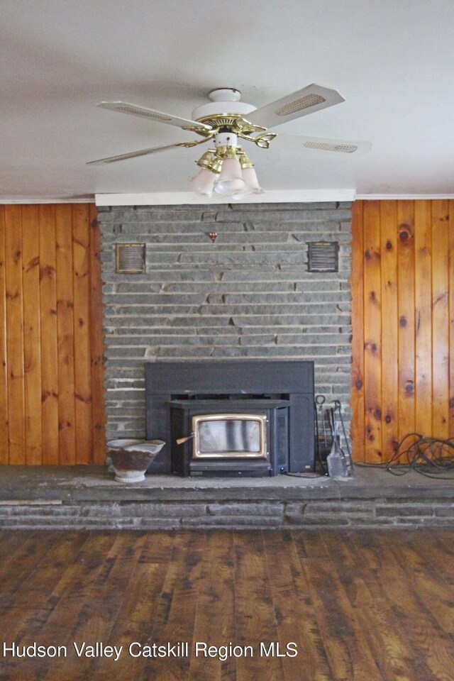 details with a wood stove, wood walls, hardwood / wood-style floors, and ceiling fan