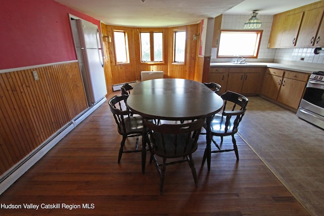 dining space featuring wooden walls, dark hardwood / wood-style floors, a baseboard heating unit, and sink