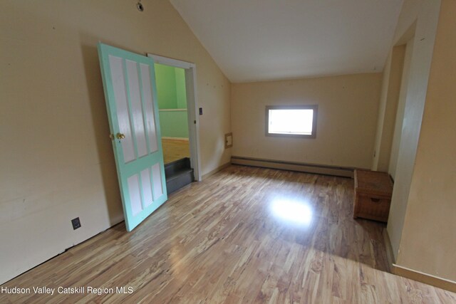 empty room featuring light hardwood / wood-style floors, vaulted ceiling, and baseboard heating