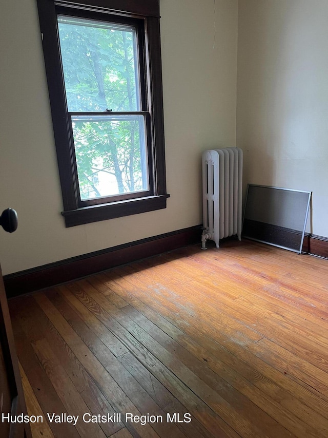 unfurnished room with plenty of natural light, wood-type flooring, baseboards, and radiator