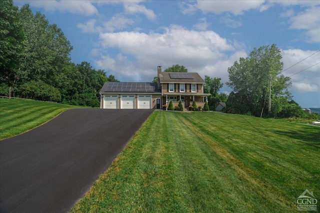  - view of front of house featuring an attached garage, driveway, a front yard, roof mounted solar panels, and a chimney