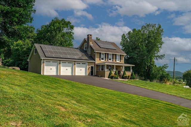  - view of front of house featuring an attached garage, asphalt driveway, roof mounted solar panels, a front yard, and covered porch