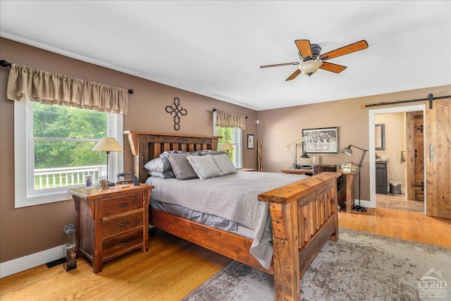  - bedroom with a barn door, light wood-style floors, baseboards, ensuite bath, and ceiling fan