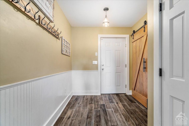  - doorway with dark wood-type flooring, a barn door, baseboards, and wainscoting