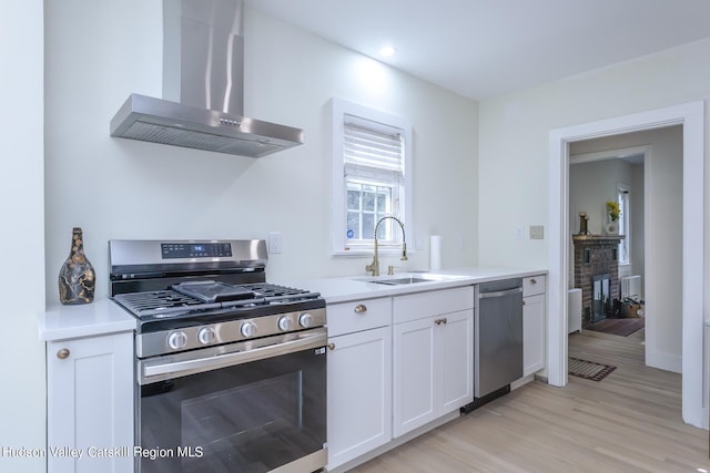 kitchen with white cabinets, wall chimney range hood, sink, light wood-type flooring, and appliances with stainless steel finishes