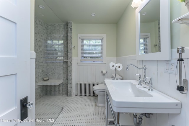 bathroom with toilet, sink, radiator, and tile walls