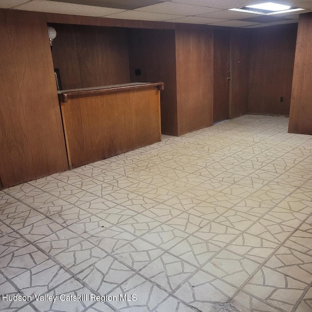 spare room featuring a drop ceiling, wooden walls, and light floors