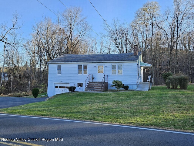 view of front facade featuring aphalt driveway, a chimney, an attached garage, and a front yard