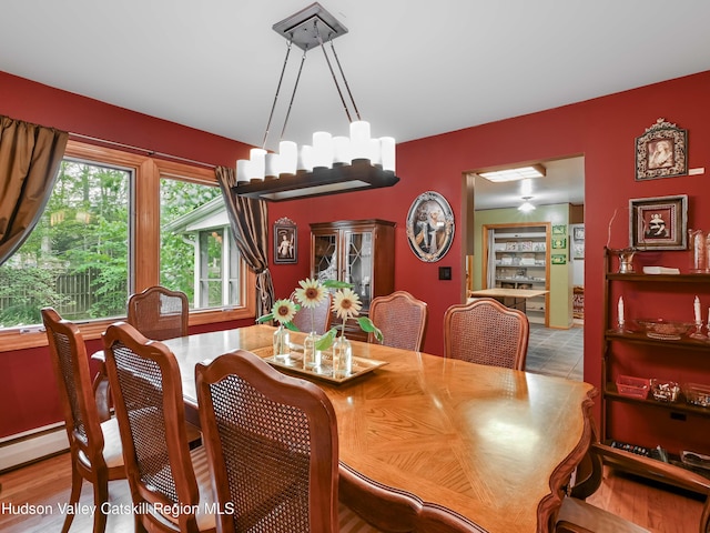 dining space featuring light wood-type flooring, a baseboard radiator, and a notable chandelier