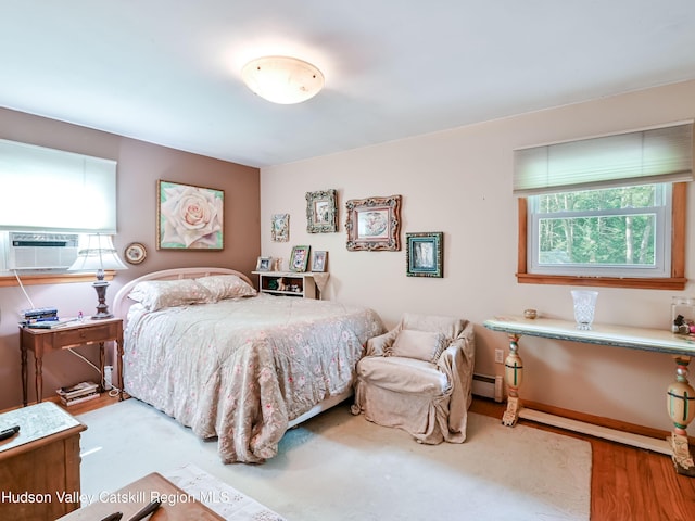 bedroom with light hardwood / wood-style floors, baseboard heating, and cooling unit