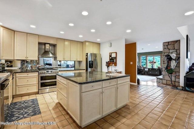 kitchen featuring appliances with stainless steel finishes, light tile patterned floors, a kitchen island, wall chimney exhaust hood, and sink