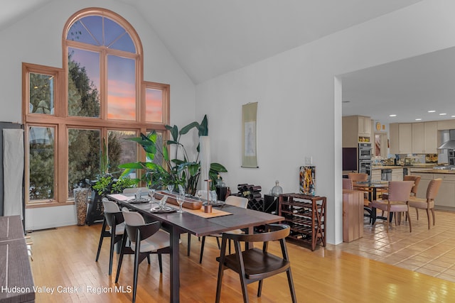 dining area with high vaulted ceiling and light hardwood / wood-style floors