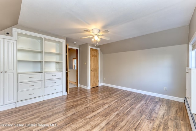 unfurnished bedroom featuring hardwood / wood-style flooring, vaulted ceiling, baseboard heating, and a closet