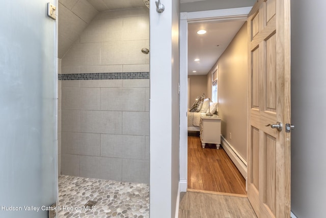 bathroom with a baseboard radiator, wood-type flooring, and tiled shower