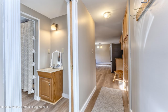 hall with baseboard heating, sink, and light hardwood / wood-style flooring