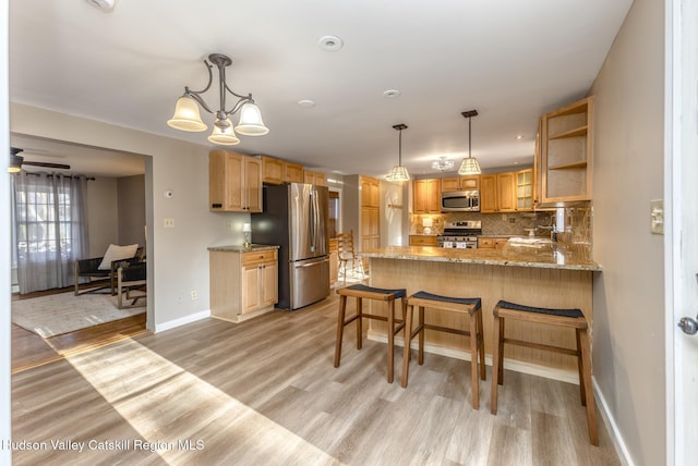 kitchen with ceiling fan with notable chandelier, decorative backsplash, kitchen peninsula, stainless steel appliances, and light hardwood / wood-style flooring