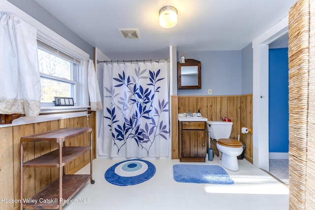 bathroom with walk in shower, wooden walls, vanity, and toilet