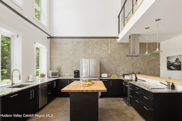 kitchen featuring hanging light fixtures, wall chimney exhaust hood, a center island, wood counters, and stainless steel appliances