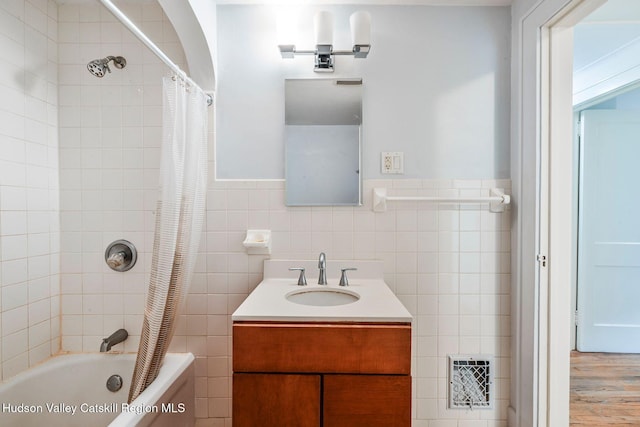 bathroom with hardwood / wood-style floors, vanity, shower / bath combination with curtain, and tile walls