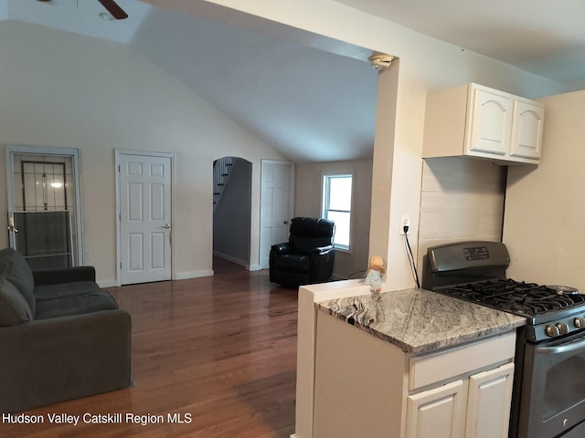 kitchen featuring dark hardwood / wood-style flooring, light stone counters, stainless steel gas range, white cabinetry, and lofted ceiling