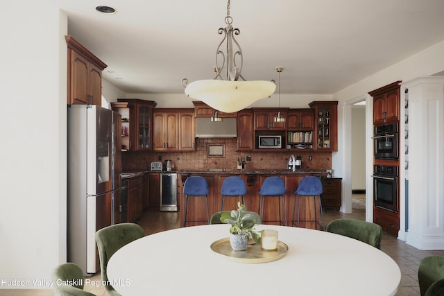 kitchen featuring hanging light fixtures, freestanding refrigerator, a center island, dark countertops, and glass insert cabinets