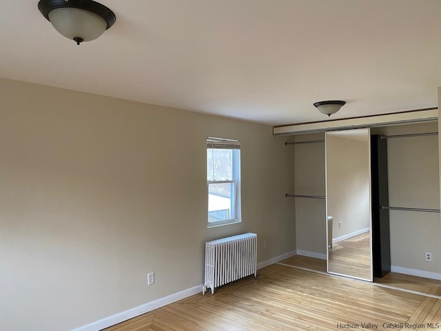 unfurnished bedroom featuring a closet, radiator heating unit, and light hardwood / wood-style floors