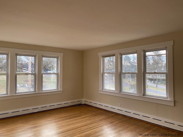 spare room featuring baseboard heating, plenty of natural light, and light wood-type flooring