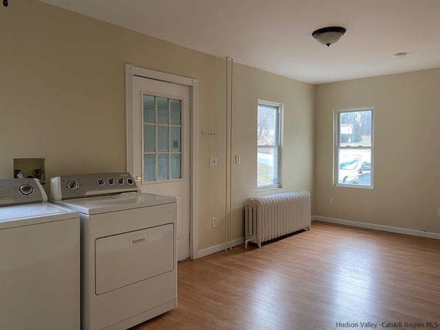 clothes washing area with light wood-type flooring, washer and clothes dryer, and radiator